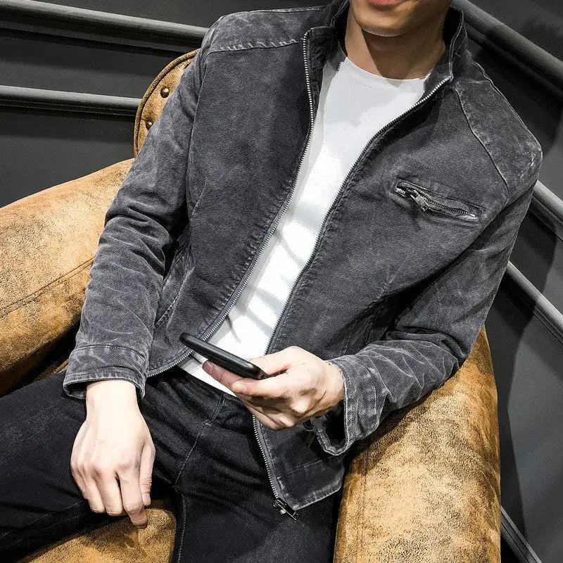 Man wearing a stylish gray denim jacket while sitting on a vintage chair, using a smartphone.